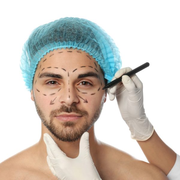 Doctor drawing marks on man's face for cosmetic surgery operation against white background